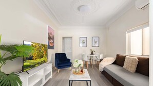 Een moderne woonkamer met een televisie, een blauwe fauteuil, een witte salontafel en een bank met een zachte plaid.