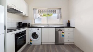 Een compacte keuken met een wasmachine, vaatwasser, oven en een raam met gordijnen.
