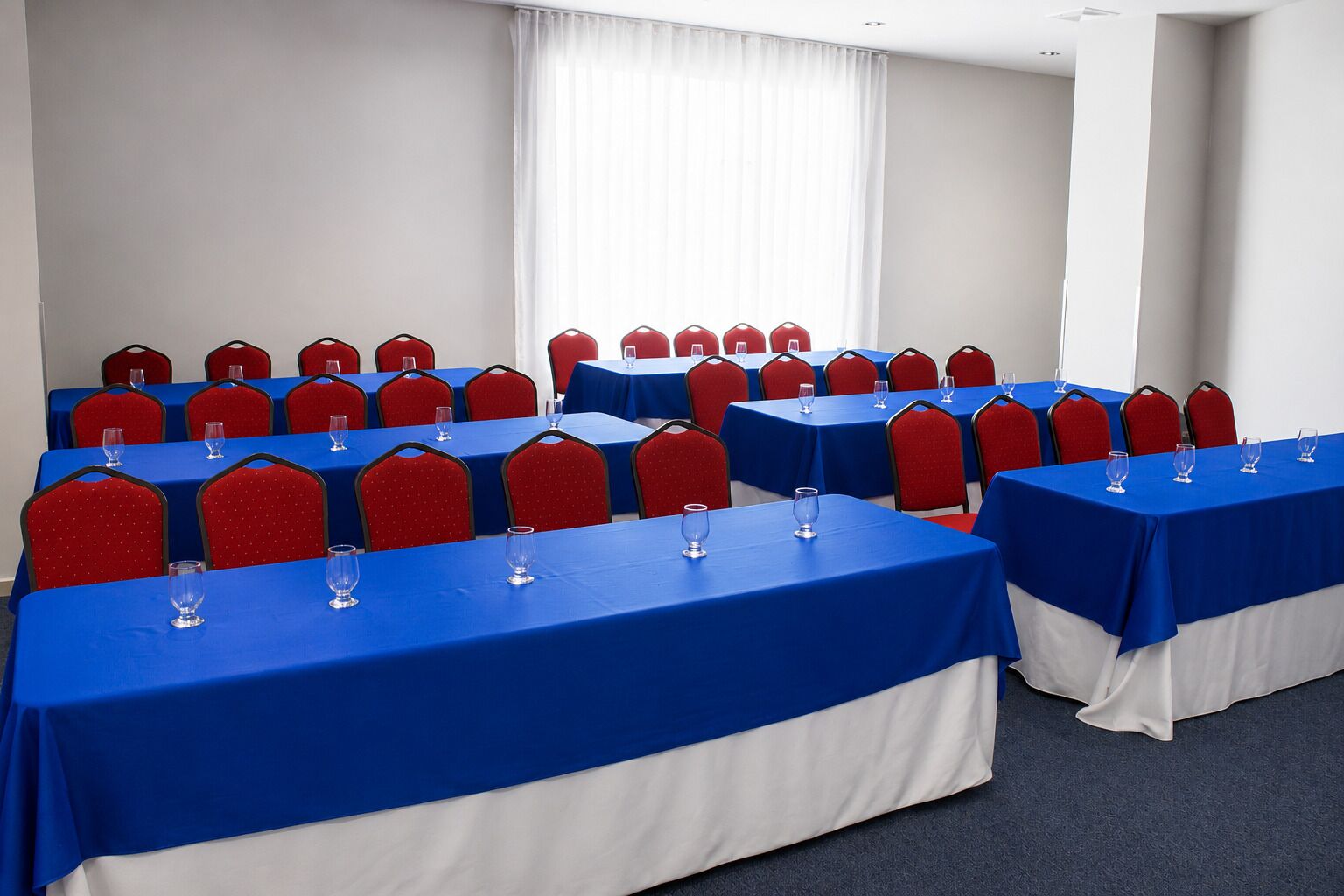 Un salón de conferencias con varias mesas y sillas, dispuestas en filas.