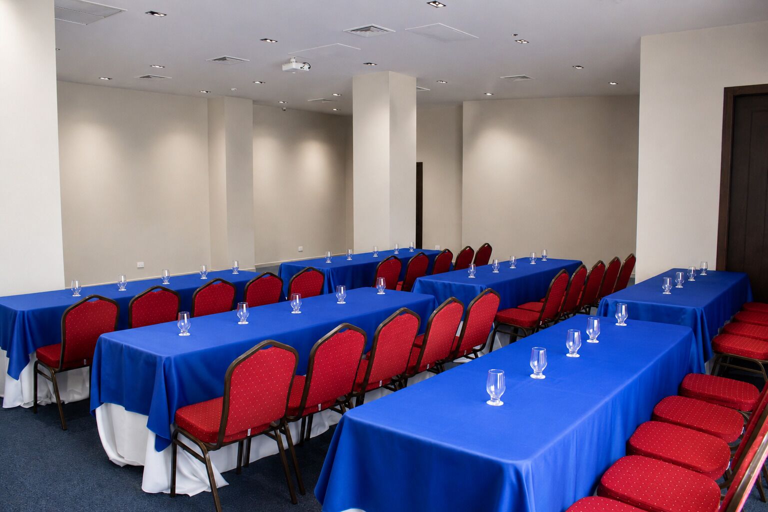 A conference room with multiple tables and chairs, arranged in rows.