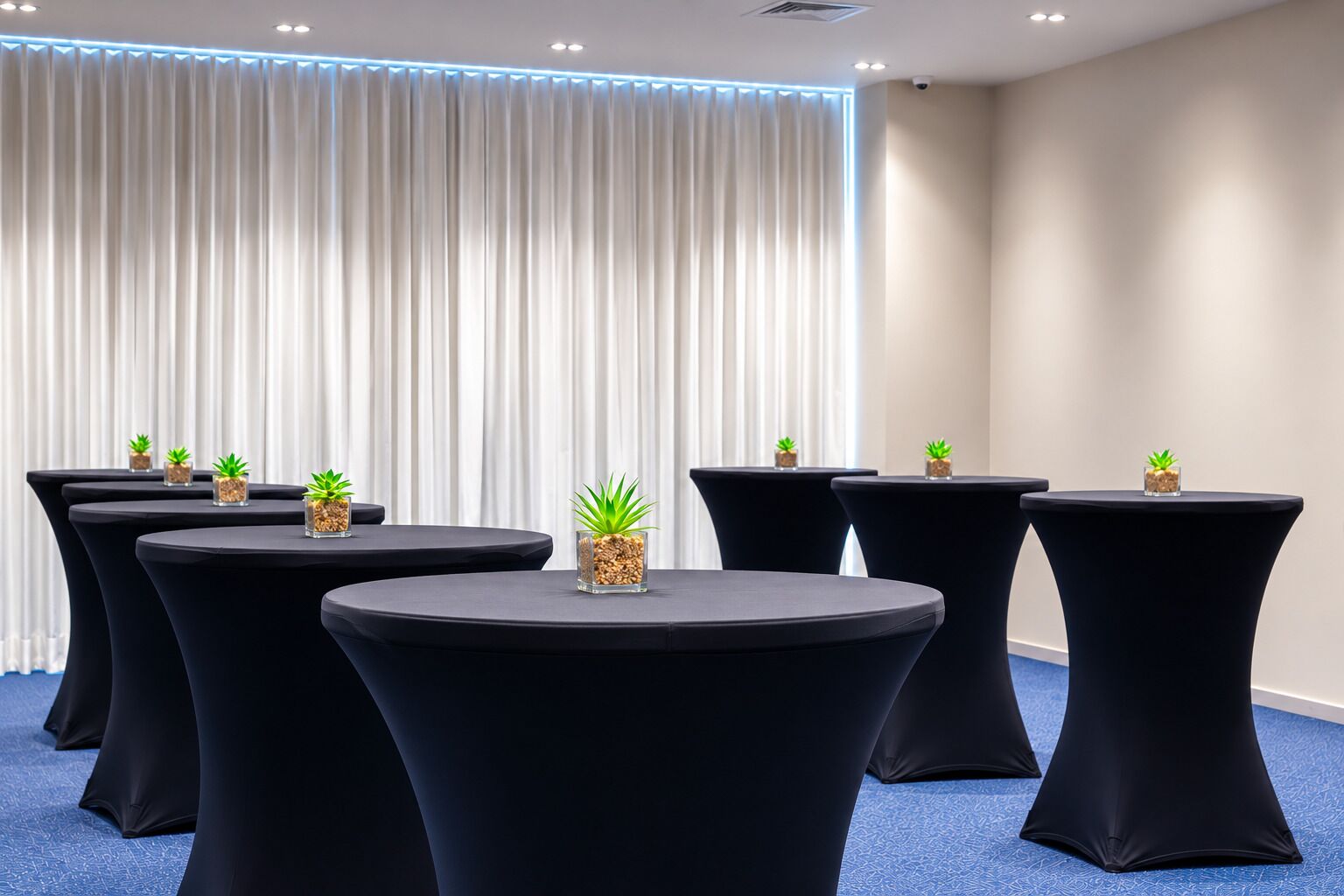 A conference room with round tables, black chairs, and small potted plants.