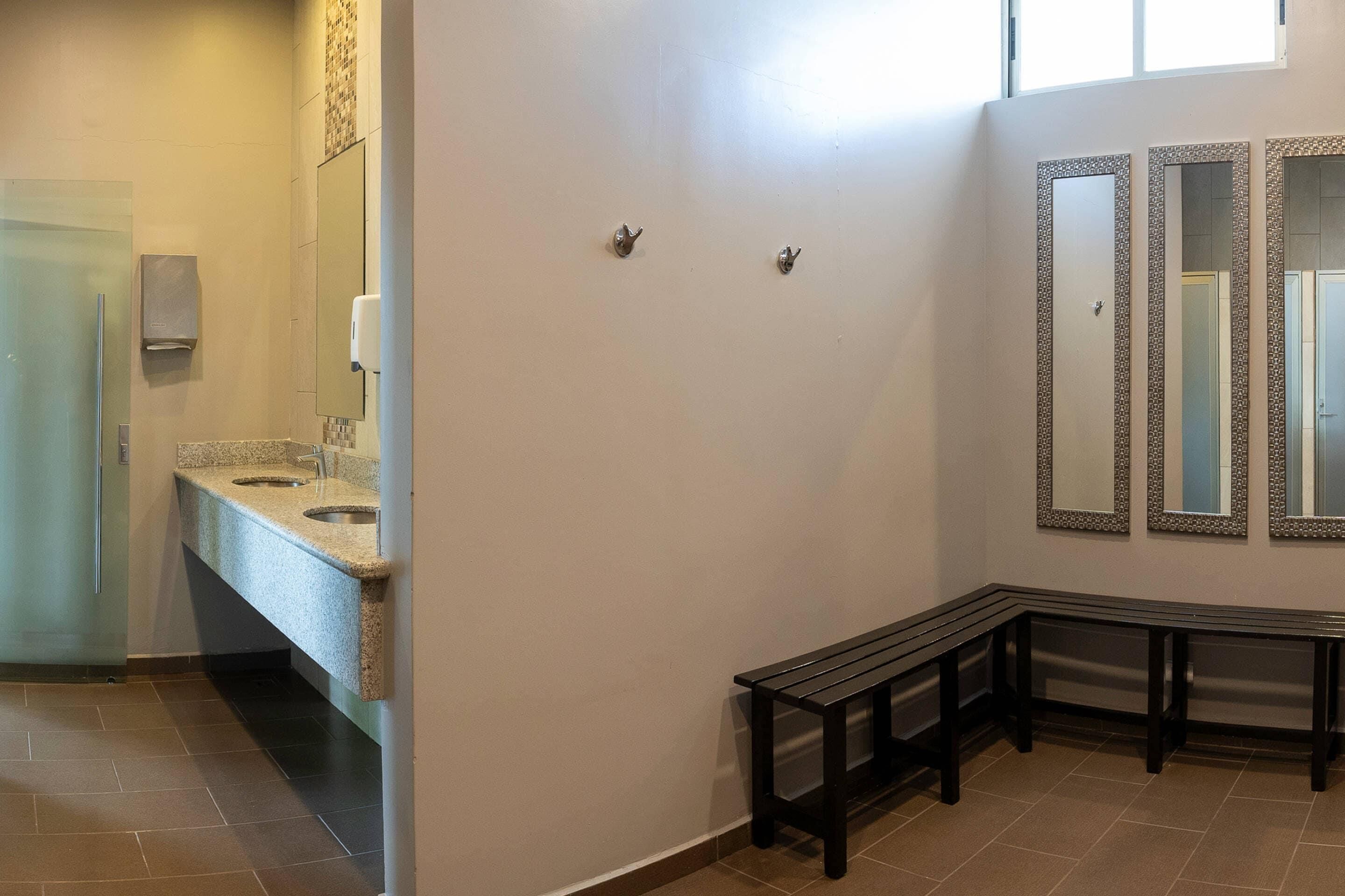 Un baño con encimera de granito, una banca y tres espejos adosados a la pared.