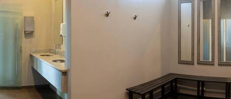 Un baño con encimera de granito, una banca y tres espejos adosados a la pared.