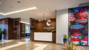 Zona de recepción de un hotel con diseño moderno, que presenta un mostrador de mármol, paneles de madera y una gran pared decorativa con cerámica.