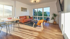 Un vaste espace de vie doté d’un plancher en bois, d’un canapé en cuir marron, d’une table à manger avec des chaises et de grandes fenêtres offrant une vue sur l’extérieur.