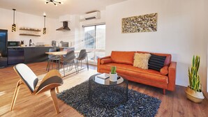 Un salon moderne avec un canapé, une table basse et des fauteuils. Il y a également un coin cuisine équipé d’un réfrigérateur et une table à manger.