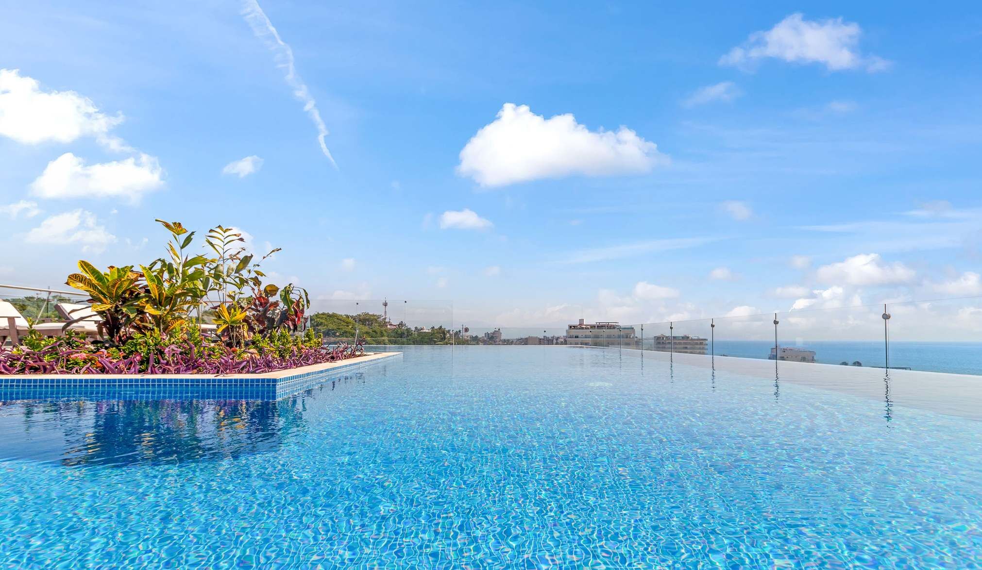 A clear blue infinity pool with a view of the sea and distant buildings.