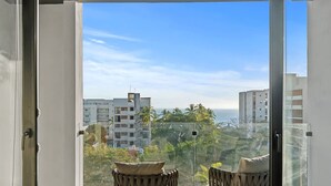 A view from a balcony with a clear sky, palm trees, and buildings in the background. - Vista Bucerias 402B - Rooftop Pool & Stunning Views (Bucerías)