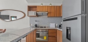 A modern kitchen with a granite countertop, stainless steel appliances, wooden cabinets, and a built-in oven. - Vista Bucerias 402B - Rooftop Pool & Stunning Views (Bucerías)