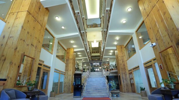 A spacious lobby with a central staircase, wooden paneling, and seating areas.