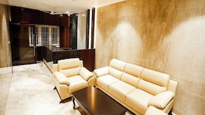 A modern living room with a beige sofa set, a dark wooden coffee table, and a marble floor. - Hotel Lakshmi Towers (Kangayam)