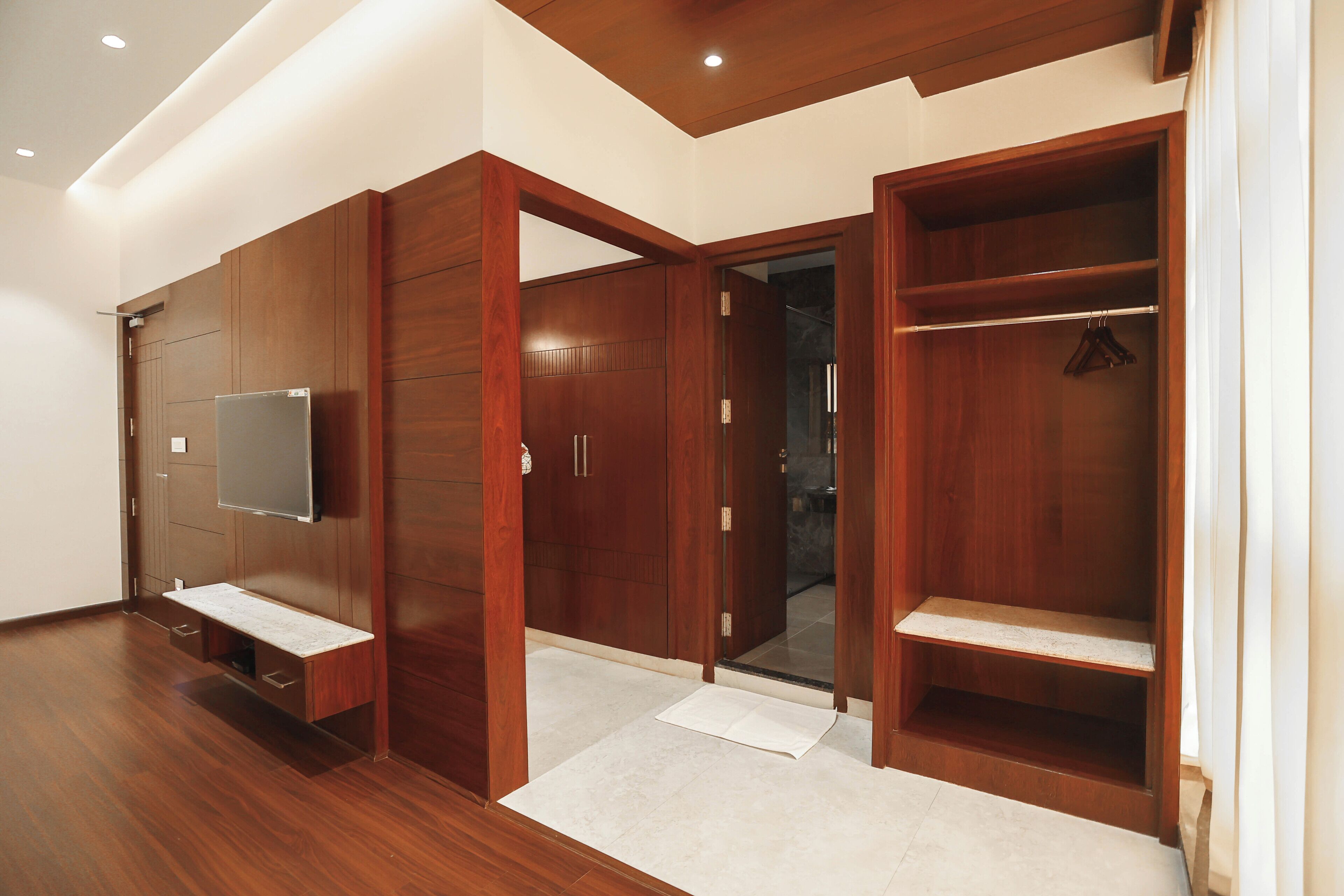 A modern room with wooden wardrobes, a flat-screen TV, and a bench.