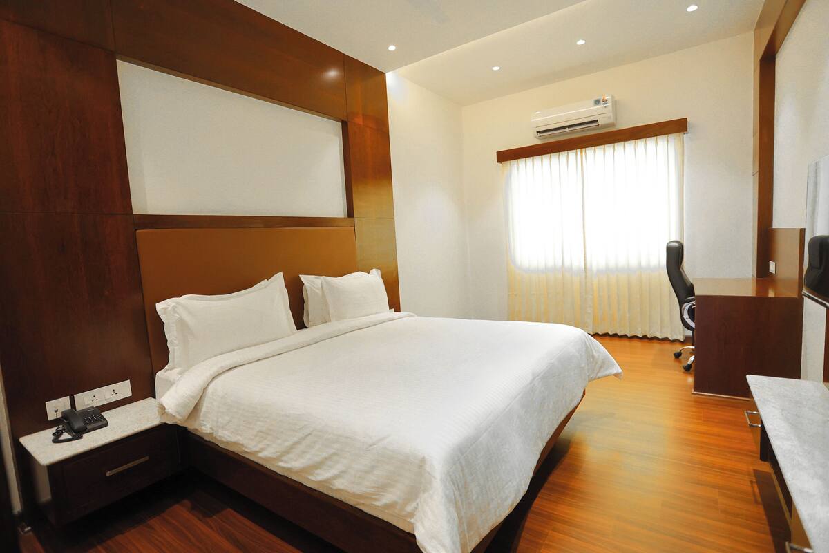 A hotel room with a large bed, a desk, and an air conditioning unit.