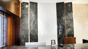 A reception desk with a marble counter, wooden paneling, and a large mirror. - Hotel Lakshmi Towers (Kangayam)