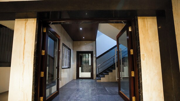 A hallway with marble flooring, glass doors, and a staircase leading to another level. - Hotel Lakshmi Towers (Kangayam)