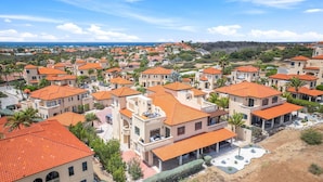 Un quartier résidentiel en bord de mer, caractérisé par des maisons aux toits orange de couleur uniforme, dont certaines sont dotées de balcons, et offrant une vue dégagée sur la mer en arrière-plan.