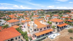 A coastal residential area with uniform orange-roofed houses, some with balconies, and a clear view of the sea in the background.