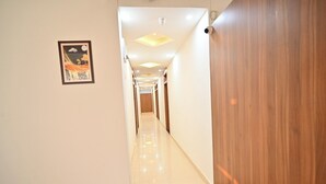 A hallway with a wooden door on the right, a framed picture on the left, and a tiled floor. - Hotel Raghav Inn  (Faizabad)