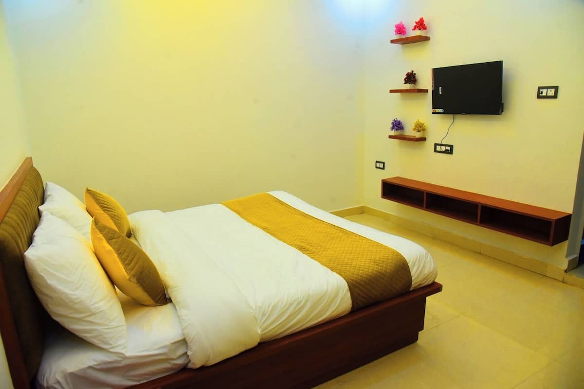 A neatly made bed with white and brown bedding, a mounted TV on the wall, and a small shelf with decorative items.