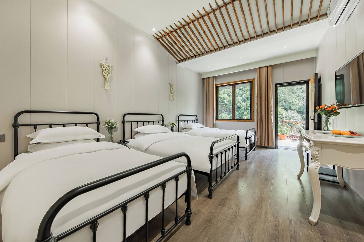 A hotel room with three beds, a desk, and a large window.