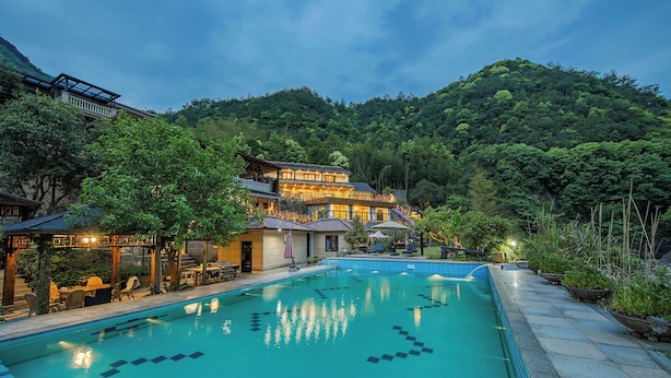 A swimming pool with a clear blue water surface, surrounded by a stone deck and lush greenery. - Hualu Yuejian Parent Child Homestay (Hangzhou)