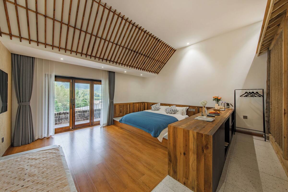 A bedroom with a wooden bed, a desk, and a large window with curtains.