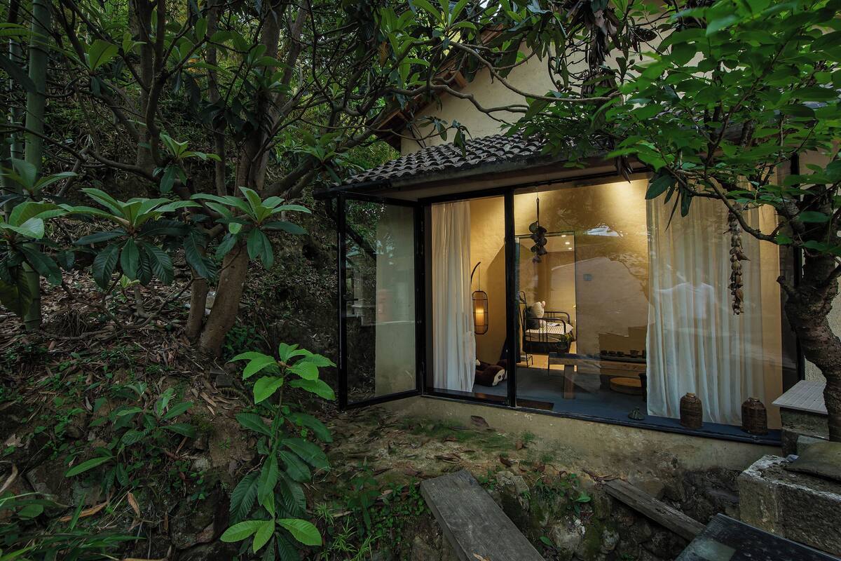 A modern house with a glass door leading to a room with a bed and a small table.