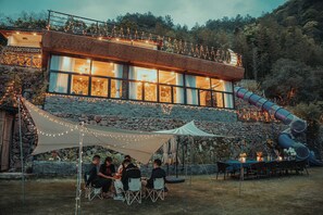 Un espace extérieur aménagé pour les repas, avec une table couverte, des guirlandes lumineuses et un toboggan.