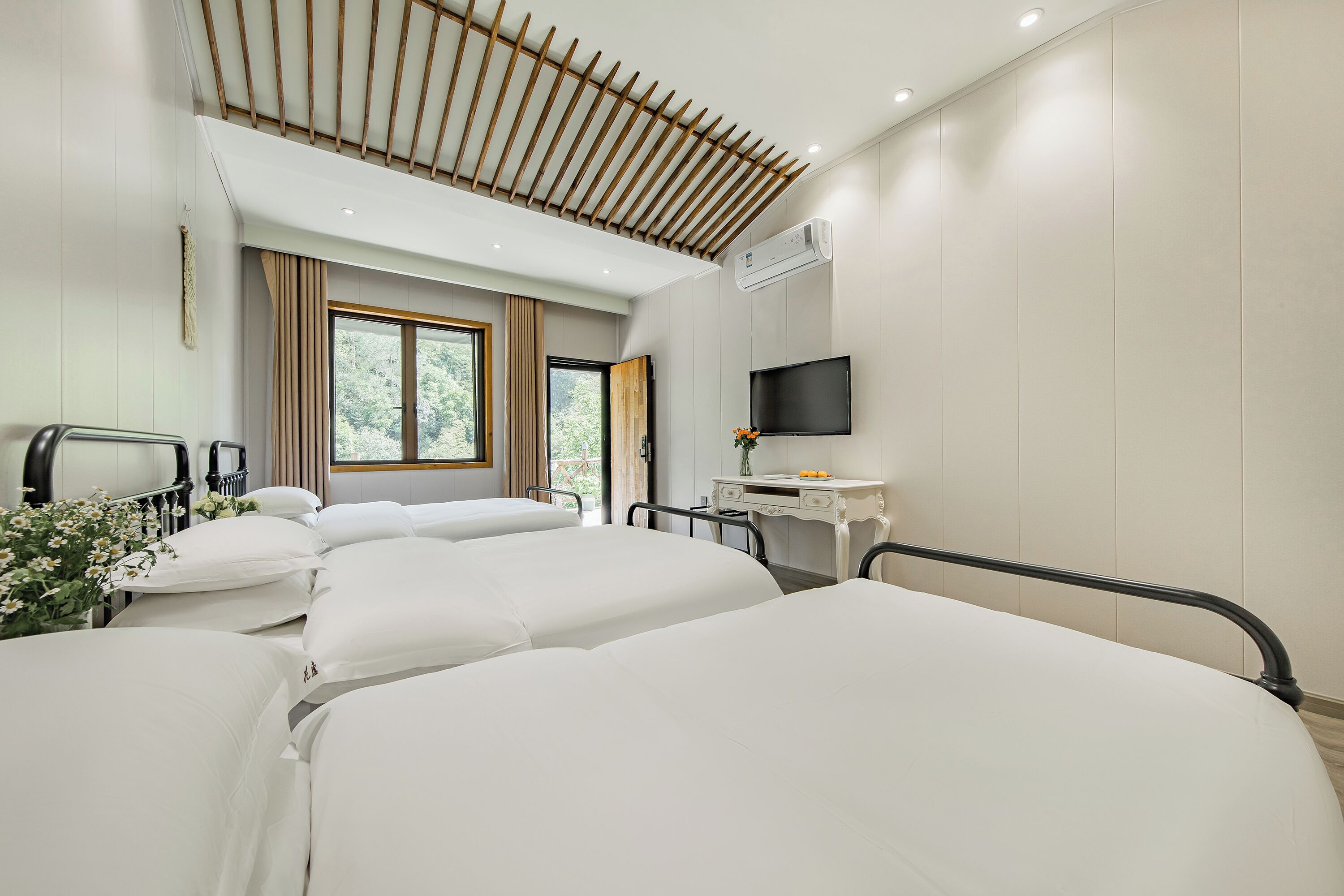 Hotelkamer met twee bedden, een bureau, een televisie en een raam met uitzicht op groen.