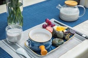 Une table dressée avec un bol de soupe, un verre de lait, un pichet de lait, une assiette contenant divers aliments et un vase avec des plantes vertes.