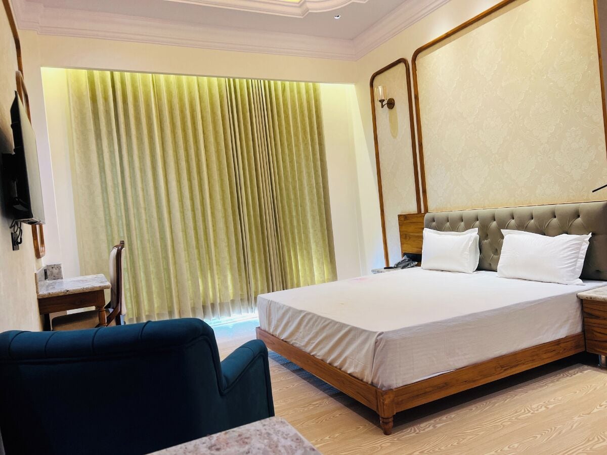 Quarto de hotel com uma cama grande, uma mesa pequena, uma cadeira e televisão na parede.