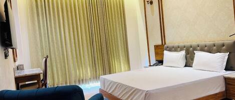 A hotel room with a large bed, a small table, a chair, and a television on the wall.