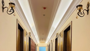 Ein langer, schmaler Hotelkorridor mit Holztüren an beiden Seiten, einem Marmorboden mit schwarzen Streifen und einem großen Fenster am Ende.