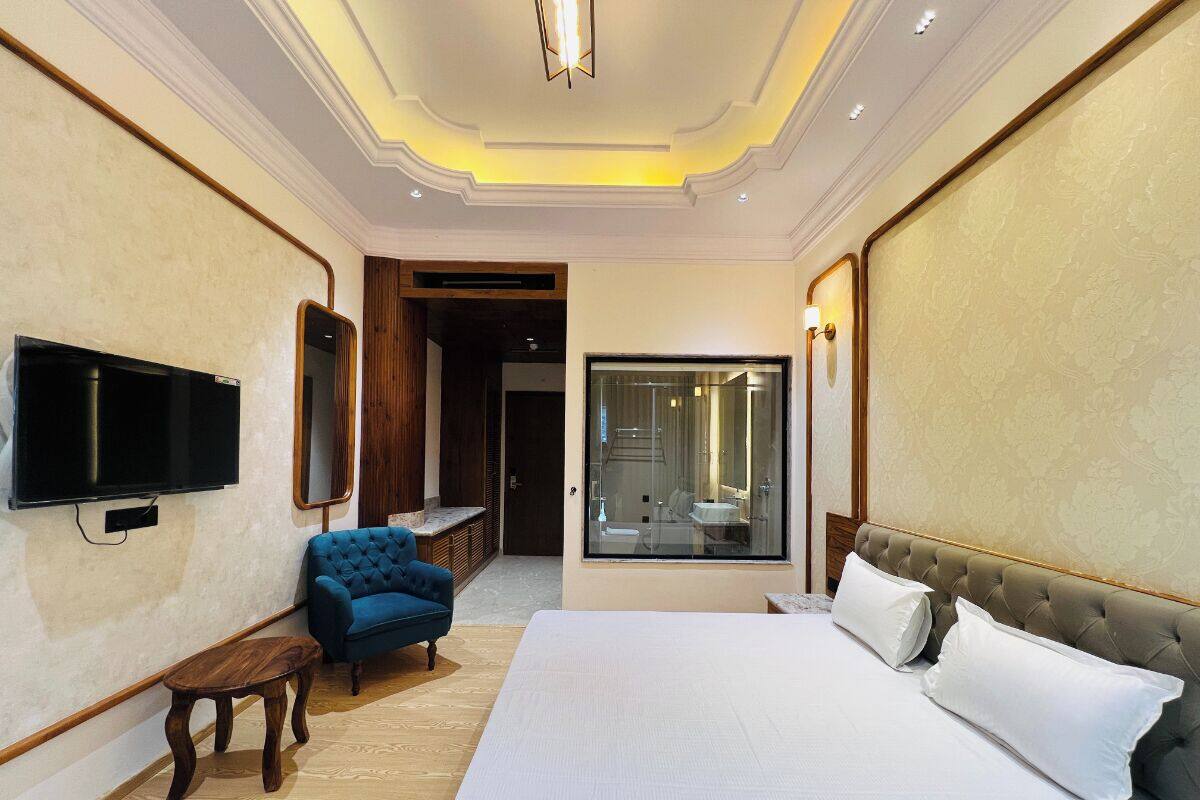 Une chambre d’hôtel avec un grand lit, une télévision, un fauteuil bleu et une salle de bain avec des parois en verre.
