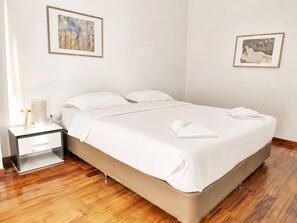 A hotel room with a bed, a nightstand, a lamp, and two framed pictures on the walls.