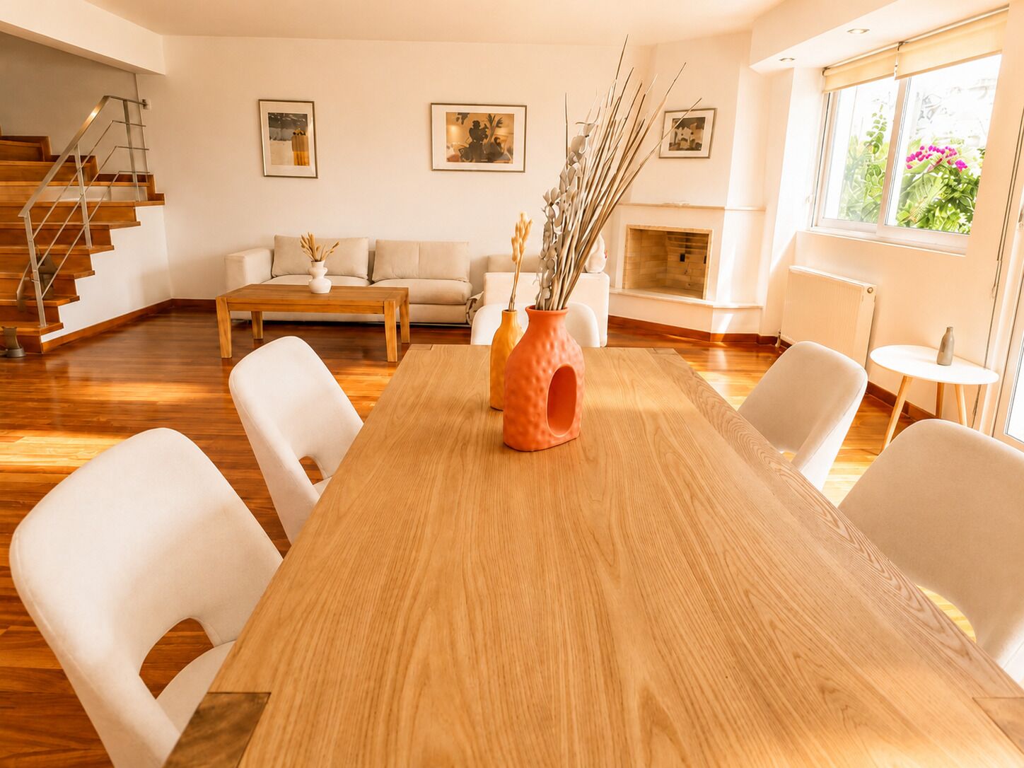 A modern living room with a wooden dining table, white chairs, a sofa, and a fireplace.
