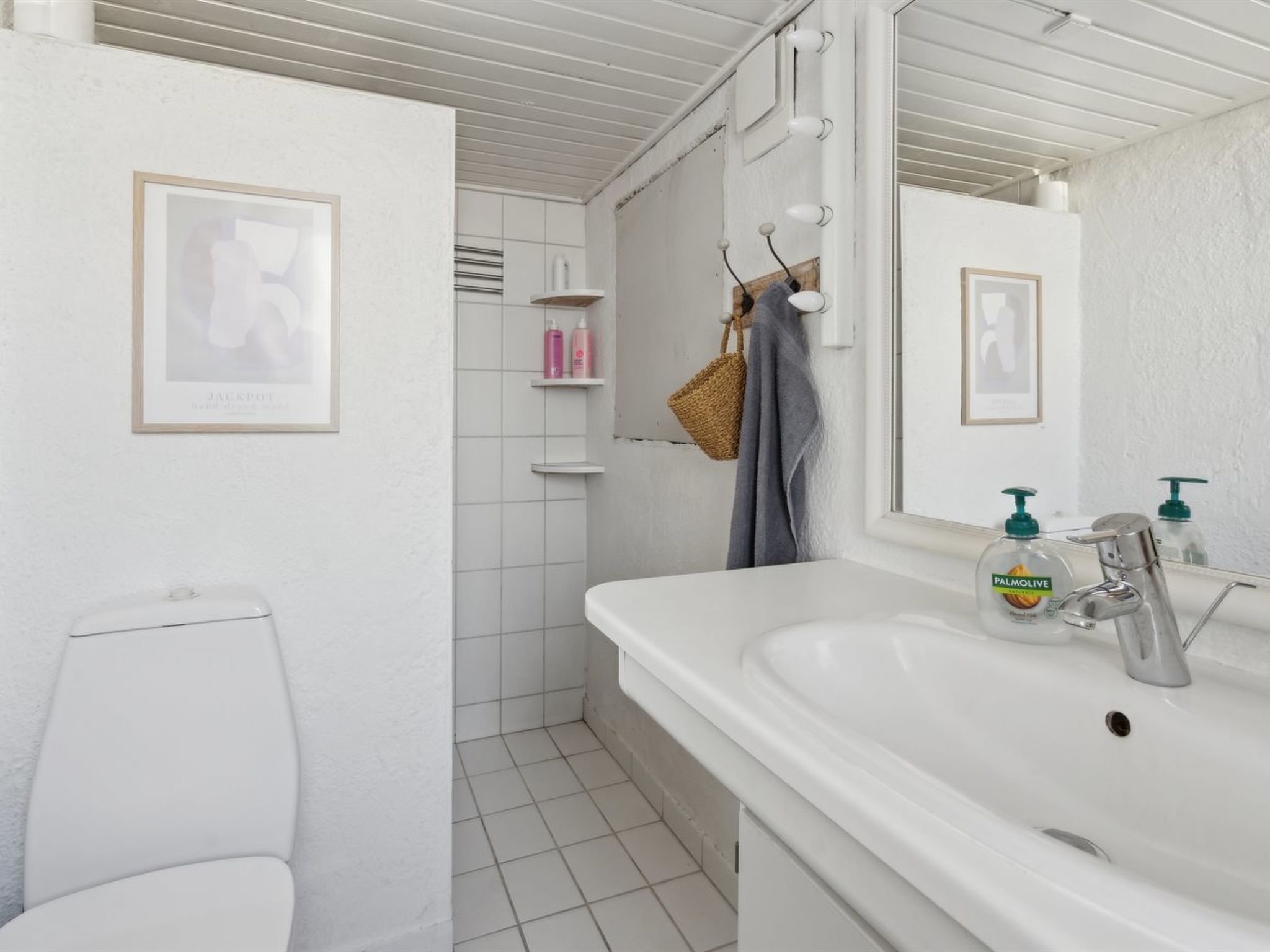 A bathroom with a white sink, mirror, and toilet. There are toiletries on the sink and a towel hanging on the wall.