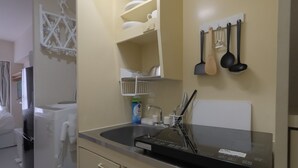 A compact kitchen with a built-in refrigerator, a sink, and a microwave. There are hanging utensils and a shelf with dishes.