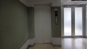 An elevator in a hallway with a green wall and a tiled floor.