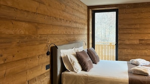A bedroom with a wooden wall, a bed with pillows, and a window. - Rustic and alpine-style apartments in Ledro Valley (Tiarno di Sotto)
