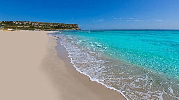 A beach with clear turquoise water and a sandy shore.