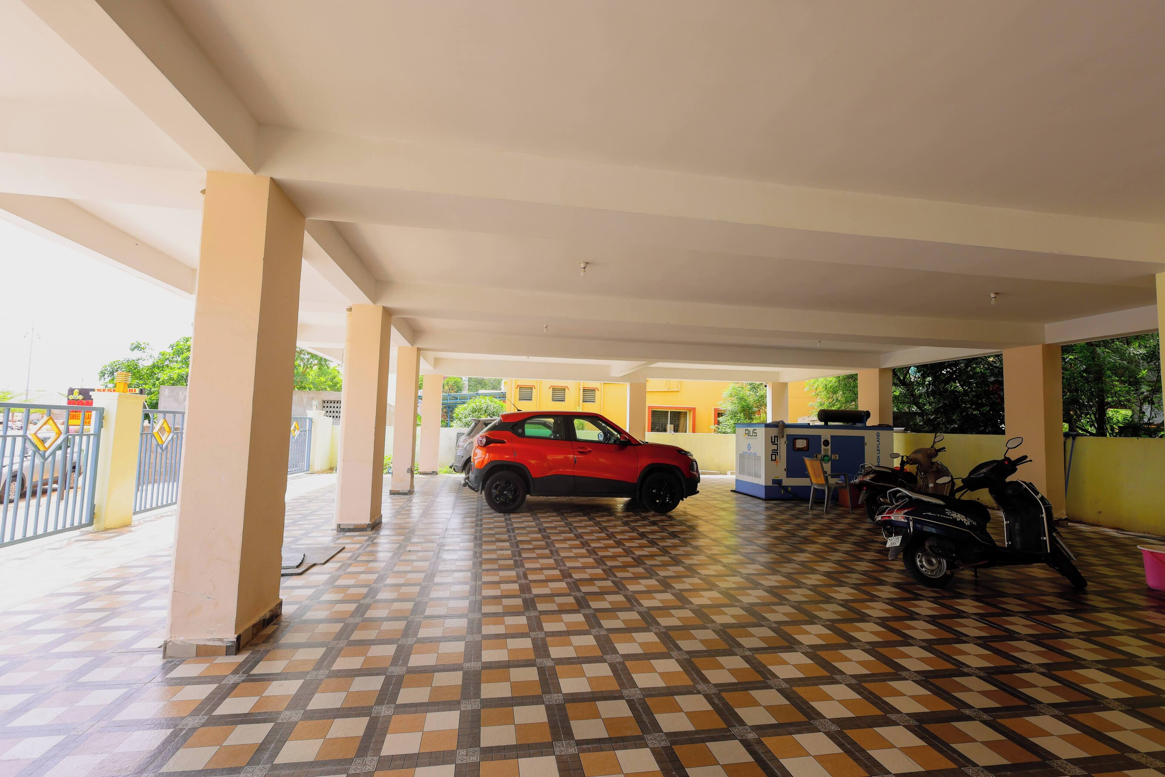 A covered parking area with a red car and a scooter, tiled floor, and a yellow building in the background.