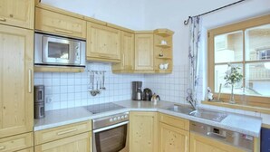 A kitchen with wooden cabinets, a stainless steel oven, a microwave, and a window with a curtain. - Quiet Alpine Cottage for 9 with Suana (Wald-Königsleiten)
