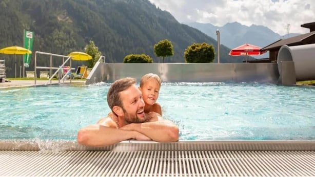 A swimming pool with a mountainous backdrop, a diving board, and umbrellas.