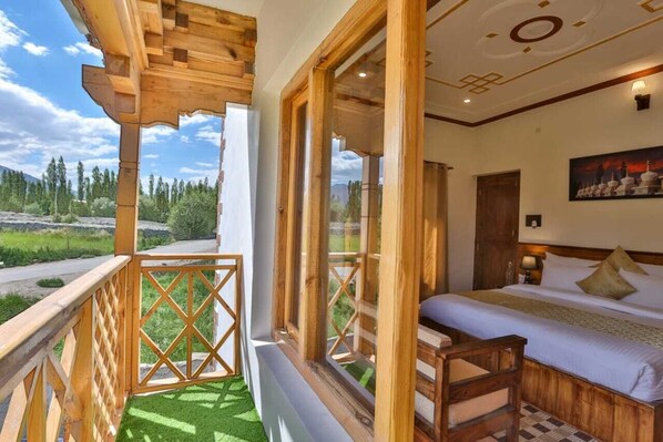 A bedroom with a large window, wooden balcony, and a bed with pillows. - Kangseng House (Leh)