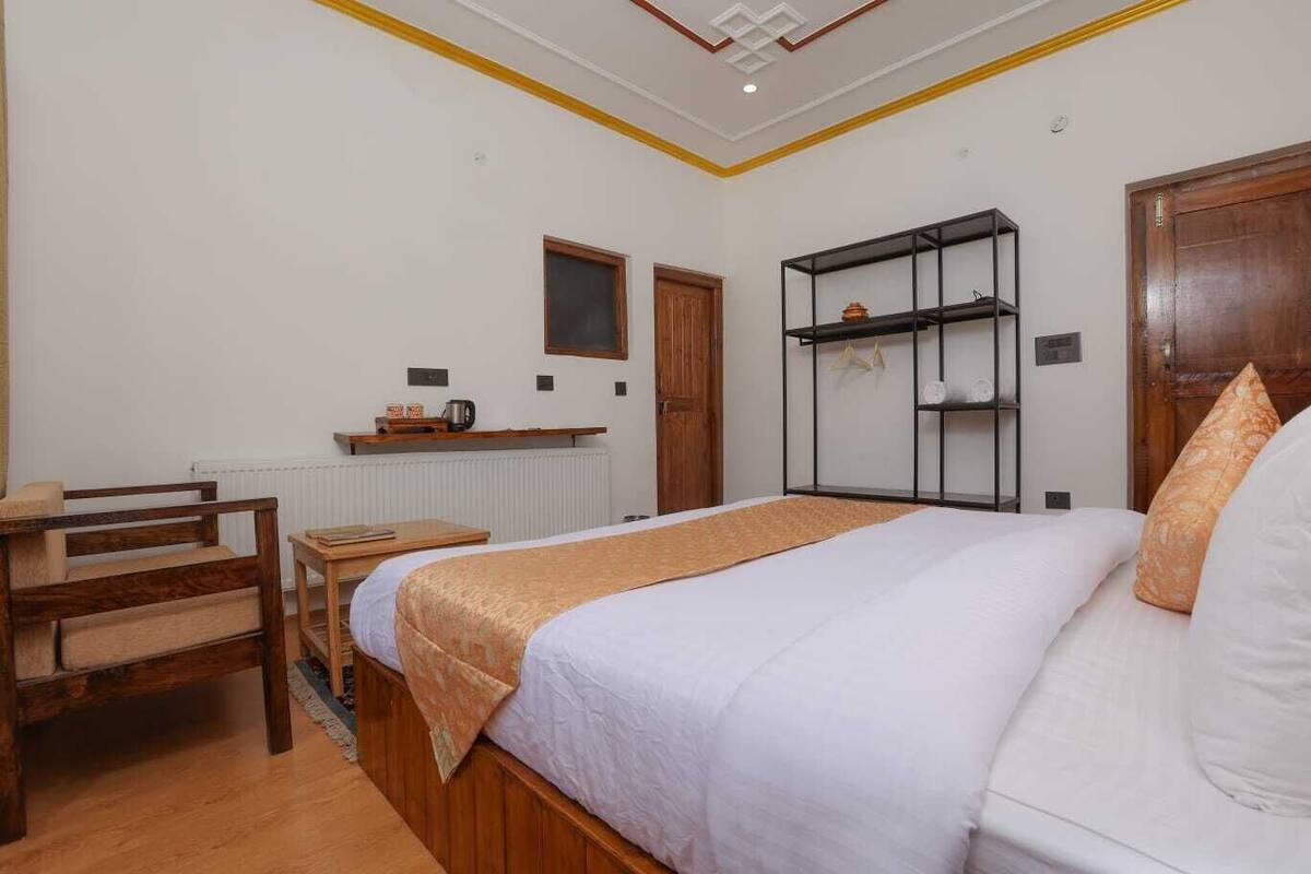 A bedroom with a bed, a desk, a chair, a radiator, a shelf with items, and a wardrobe.