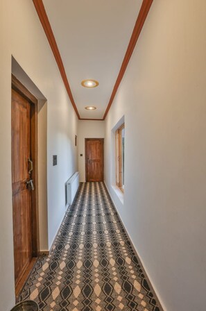 A narrow hallway with patterned flooring, wooden doors, and a window on the right. - Kangseng House (Leh)