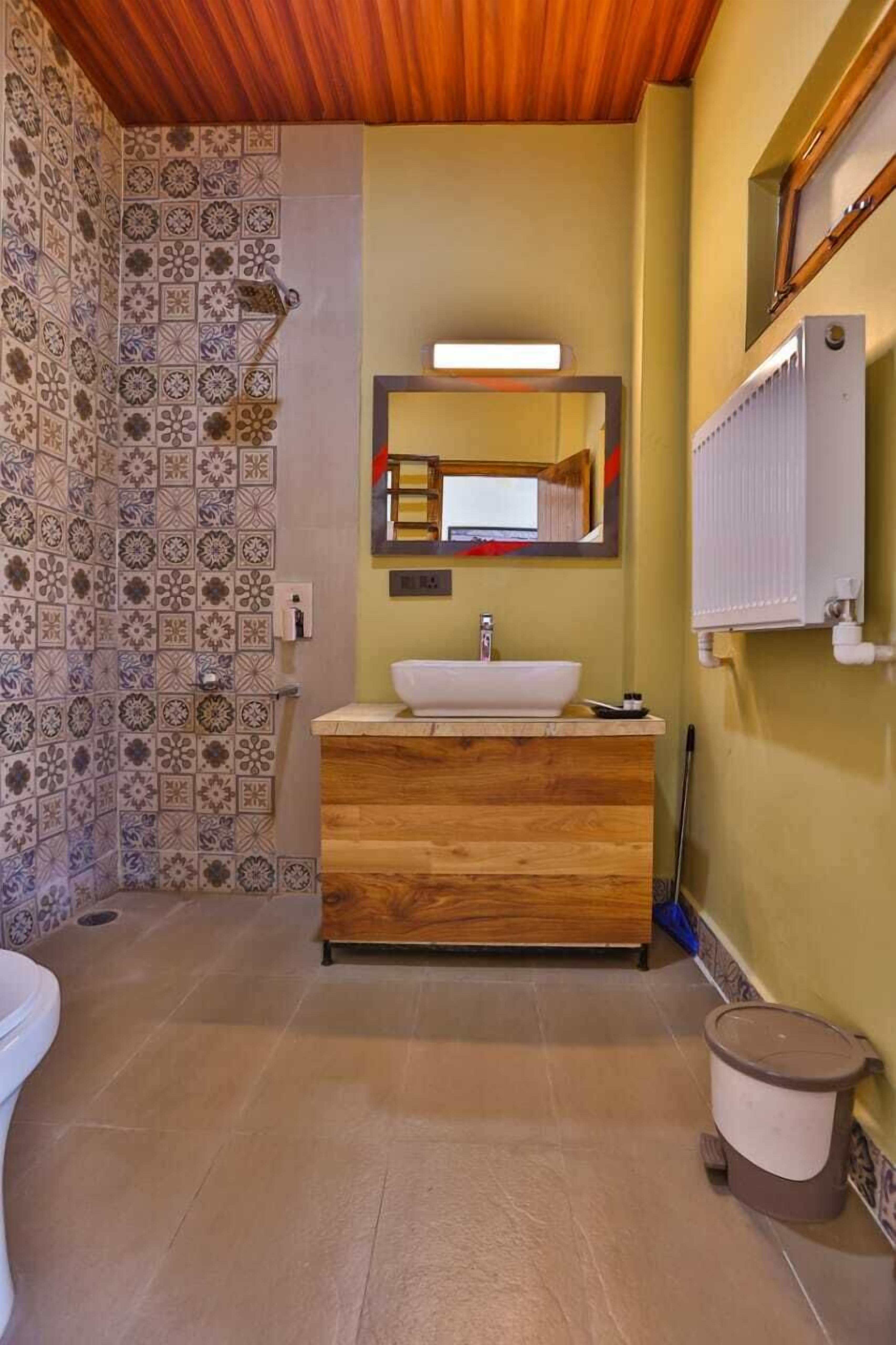 A bathroom with a wooden vanity, a white sink, a mirror, and patterned tiles on the walls.