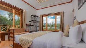 A bedroom with a large bed, a wooden desk, and a view of the outdoors through large windows. - Kangseng House (Leh)