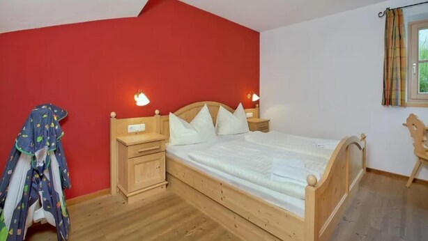 A bedroom with a wooden bed, nightstands, a red wall, and a window with curtains.